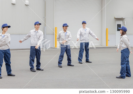 A group of workers doing exercises in front of a factory A group of workers doing exercises in front of a factory 130095990