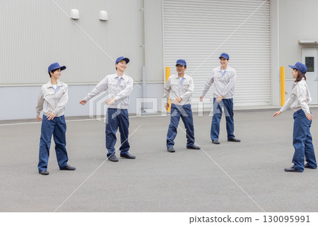 A group of workers doing exercises in front of a factory A group of workers doing exercises in front of a factory 130095991