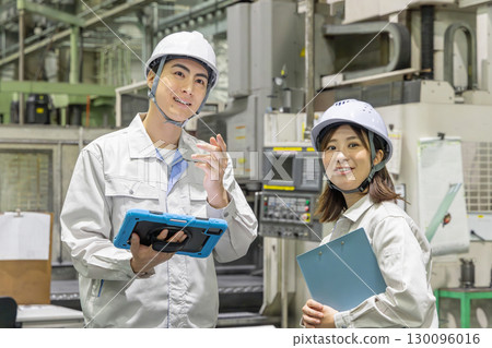 Male and female workers inspecting factory machines with a tablet 130096016