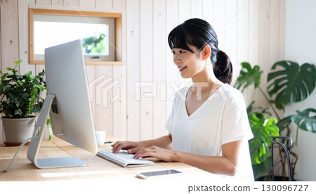 一位年輕的日本女性在明亮的夏日室內的木桌上用電腦工作 130096727