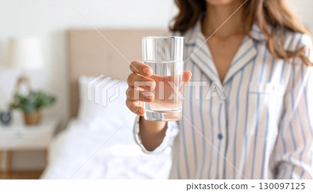 Woman in pajamas holding a glass of water in her bedroom Woman in pajamas holding a glass of water in her bedroom 130097125