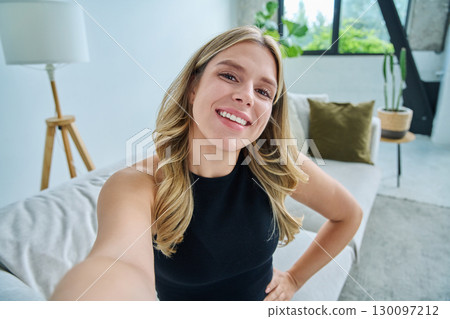 Selfie portrait happy beautiful young woman in home interior 130097212