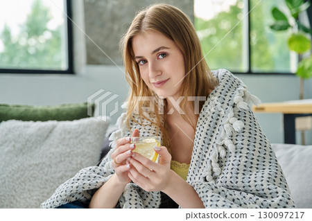 Young woman under blanket with cup with lemon, at home on sofa 130097217