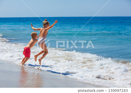 Happy kids have fun in sea surf on white sand beach. Couple of children sit in water pool. Travel lifestyle, swimming activities in family summer camp. Vacations on tropical island. 130097283