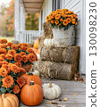 Cozy fall farmhouse porch with pumpkins, mums, and hay bales 130098230