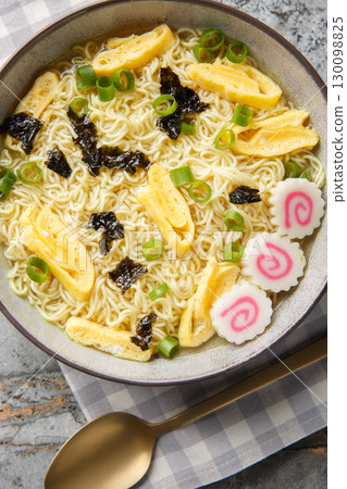 Saimin soup made from egg noodles and a dashi broth with great toppings like nori, omelette, kamaboko and green onions closeup in the plate. Vertical top view 130098825