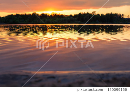 Stunning sunset over a peaceful lake, reflecting vibrant orange hues on rippling water 130099166