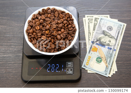 A white bowl filled with roasted coffee beans sits on a digital scale displaying A white bowl filled with roasted coffee beans sits on a digital scale displaying 130099174