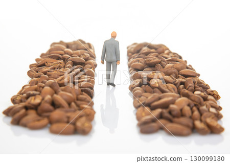 A symbolic stock photo of a miniature figure in a suit walking between piles of coffee beans 130099180