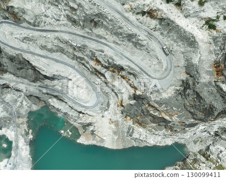 Aerial view truck in motion through terraced quarry levels during stone extraction. Mining technology, land use transformation, and corporate responsibility in heavy industry. Open pit mine industry. 130099411