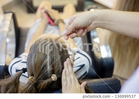 In a cozy salon, a stylist delicately braids a clients hair, showcasing intricate techniques. The atmosphere is serene, ideal for pampering and transformation. 130099537
