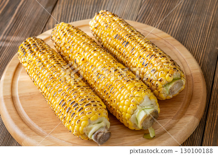 Three grilled corn cobs with char marks resting on wooden cutting board Three grilled corn cobs with char marks resting on wooden cutting board 130100188
