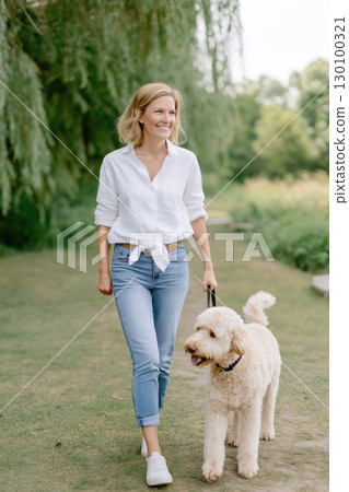A woman strolls along a path with her fluffy dog 130100321