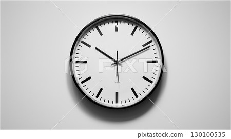 A modern wall clock with a black frame and a numberless face hangs in the center of a white wall. A modern wall clock with a black frame and a numberless face hangs in the center of a white wall. 130100535