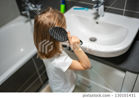Little girl brushing her hair with a detangling hairbrush in the bathroom. Concept of daily self-care and developing independence in childhood. 130101431