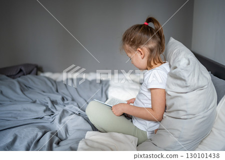 Little girl sitting on her parents bed and reading a book in the bedroom. Concept of quiet time, concentration and love for reading in early childhood. Little girl sitting on her parents bed and reading a book in the bedroom. Concept of quiet time, concentration and love for reading in early childhood. 130101438