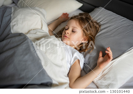 Little girl sleeping peacefully in a large adult bed. Concept of childhood vulnerability, safety and innocence in a grown-up world. 130101440