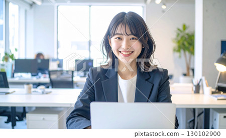A female employee in a suit smiling while operating a laptop 130102900