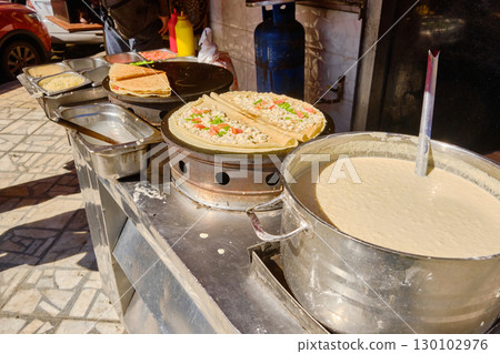 Street food vendor preparing savory crepes on open griddle 130102976