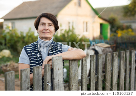 Mature woman standing relaxed near fence in backyard smiling 130103127