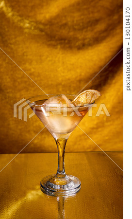 Golden cocktail with ice cube and dried citrus slice on reflective background 130104170