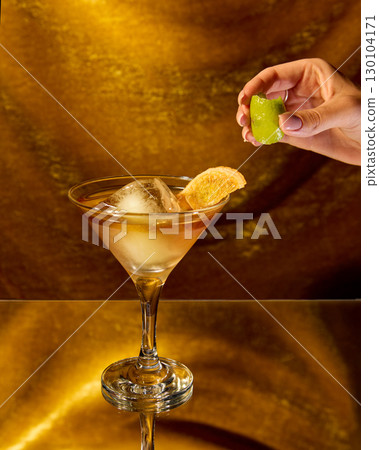 Cocktail with lime and dried orange slice in martini glass on golden reflective surface Cocktail with lime and dried orange slice in martini glass on golden reflective surface 130104171