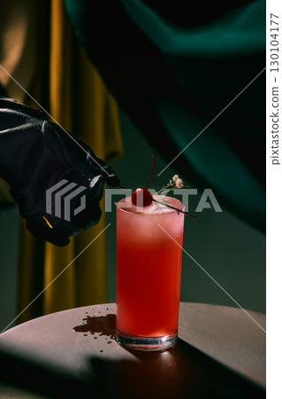 Red cocktail with cherry garnish and black glove hand on table Red cocktail with cherry garnish and black glove hand on table 130104177