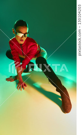 Dynamic woman in red jacket and futuristic shades crouching with dramatic green lighting Dynamic woman in red jacket and futuristic shades crouching with dramatic green lighting 130104203