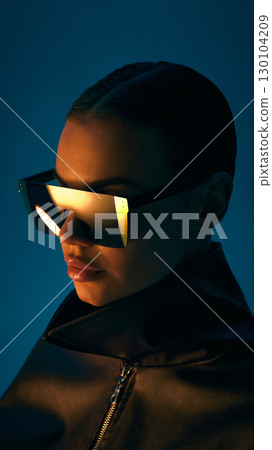 Woman in futuristic sunglasses with reflection and leather jacket on dark background 130104209