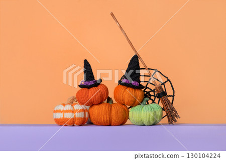 Knitted green orange pumpkins, knitted black spider web and a witch's broom on gradient background, front view. Halloween concept. Handmade knitted toys for children and holiday home decor. Knitted green orange pumpkins, knitted black spider web and a witch's broom on gradient background, front view. Halloween concept. Handmade knitted toys for children and holiday home decor. 130104224