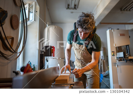 Skilled carpenter apply full attention to precision work on jointer machine processing wooden beam Skilled carpenter apply full attention to precision work on jointer machine processing wooden beam 130104342
