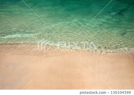 Serene Beach Shoreline. Clear turquoise water gently laps against a sandy beach. 130104399