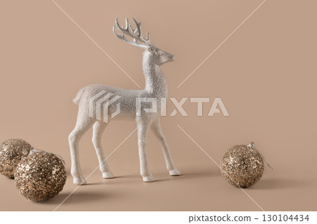 Christmas golden shiny baubles and silver deer figurine stands against beige background. Mocha Mousse. Copy space. Xmas card 130104434