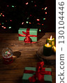 Green Presents Sit by Glowing Candles on a Rustic Wooden Table 130104446