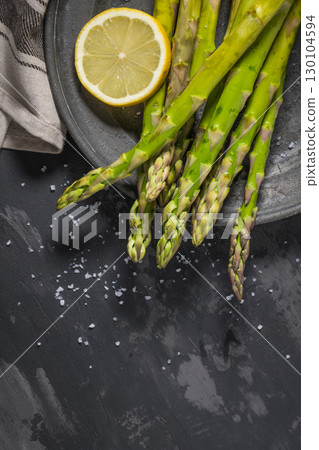 Bundle of young raw uncooked organic green asparagus with sliced lemon 130104594