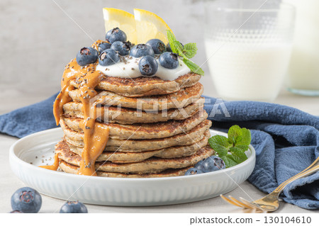 Healthy summer breakfast, homemade classic american pancakes with fresh blue berries, lemon, yogurt and peanut butter. Morning light grey stone background. 130104610