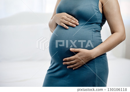 Close up of pregnant woman in blue dress gently holding her baby bump with both hands in bedroom Close up of pregnant woman in blue dress gently holding her baby bump with both hands in bedroom 130106118