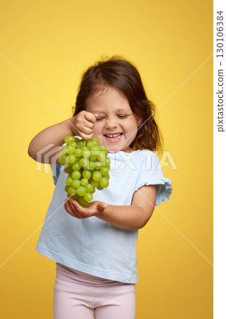 funny Caucasian little child girl holding bunch of green grapes on yellow background funny Caucasian little child girl holding bunch of green grapes on yellow background 130106384