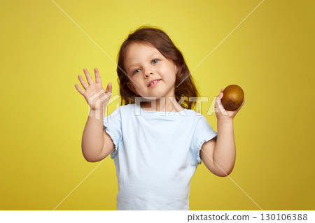 funny little child girl holding kiwi fruit on yellow background 130106388