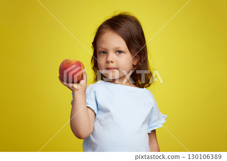 Portrait of brunette little child girl with peach on yellow background 130106389