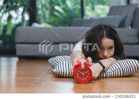 Young asian woman reaching over to turning off alarm clock while lying on the floor in living room at home. 130106831