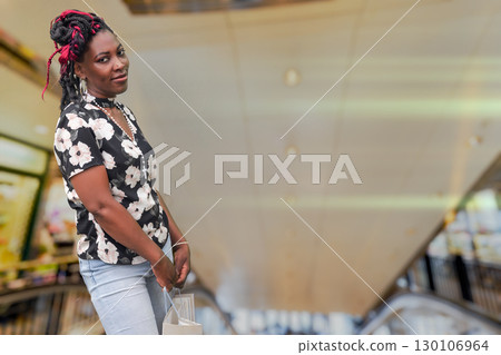 African American woman shopping in mall with bag near escalator 130106964