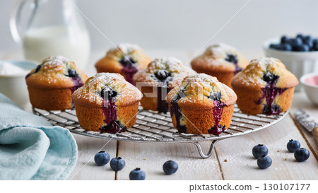 Freshly baked blueberry muffins on cooling rack, dusted with powdered sugar and surrounded by berries and milk on rustic wooden table 130107177