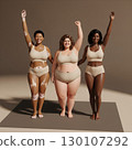 Three diverse young adult females, with varying body types and skin conditions, pose happily in neutral underwear, arms raised. Generative AI. 130107292