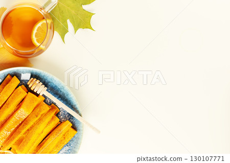 Baked pumpkin slices with cinnamon, honey and herbal tea on a white background with autumn leaves and copy space. Vegan dessert, healthy food. Autumn food and comfort meal. Flat lay Baked pumpkin slices with cinnamon, honey and herbal tea on a white background with autumn leaves and copy space. Vegan dessert, healthy food. Autumn food and comfort meal. Flat lay 130107771