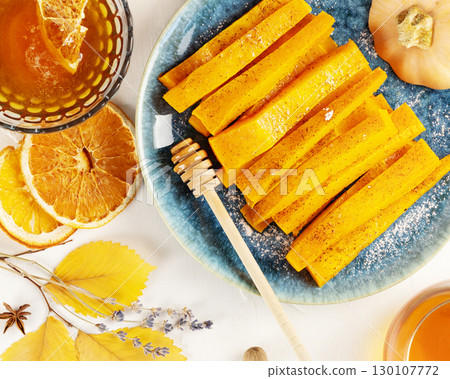 Baked pumpkin slices with cinnamon, honey and dried oranges with herbal tea on a white background with autumn leaves. Vegan dessert, healthy food. Autumn food, comfort meal. Flat lay Baked pumpkin slices with cinnamon, honey and dried oranges with herbal tea on a white background with autumn leaves. Vegan dessert, healthy food. Autumn food, comfort meal. Flat lay 130107772