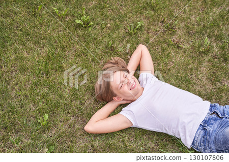 Caucasian young girl relaxing on grass in white t shirt and jeans with hands 130107806