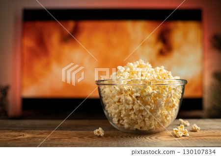 A glass bowl of popcorn and remote control in the background the TV works A glass bowl of popcorn and remote control in the background the TV works 130107834
