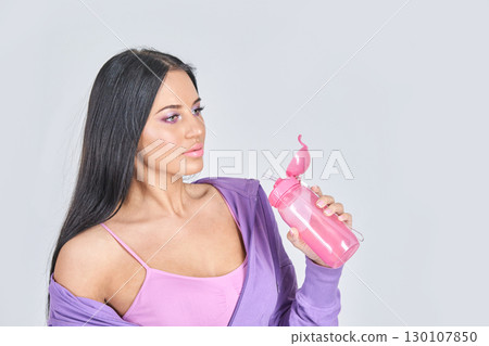 Young caucasian female drinking from pink bottle in casual purple outfit against Young caucasian female drinking from pink bottle in casual purple outfit against 130107850