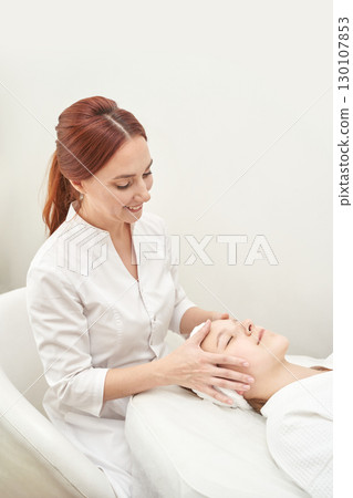 Caucasian female spa therapist performing facial massage on young woman in relax 130107853